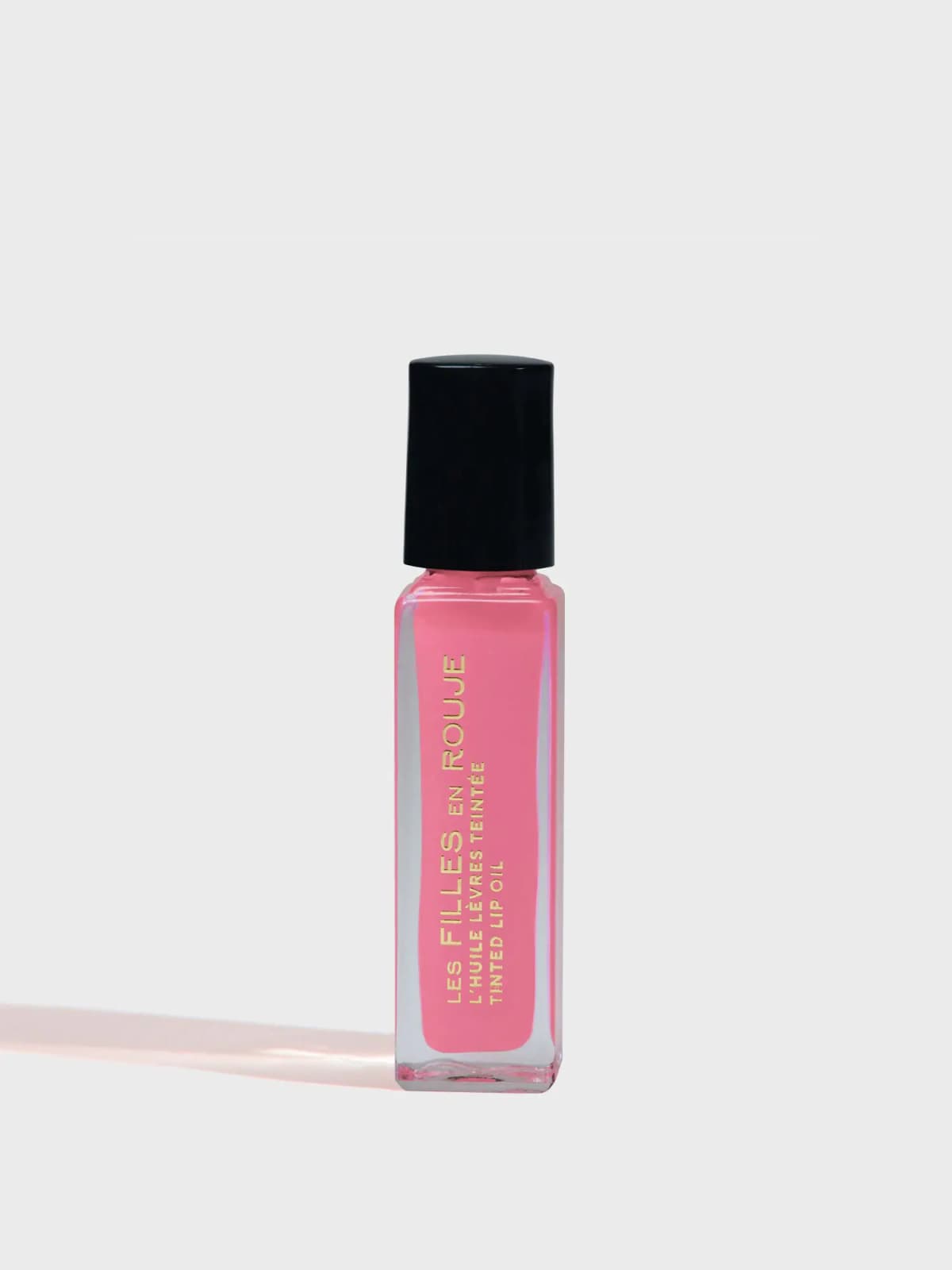 Les Filles en Rouje tinted lip oil in a square glass bottle of pink liquid with gold lettering and a black cap