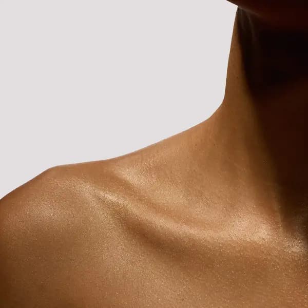 Portofino '97 Golden Shimmer Body Oil applied to a shoulder and collarbone, giving a glowing golden sheen
