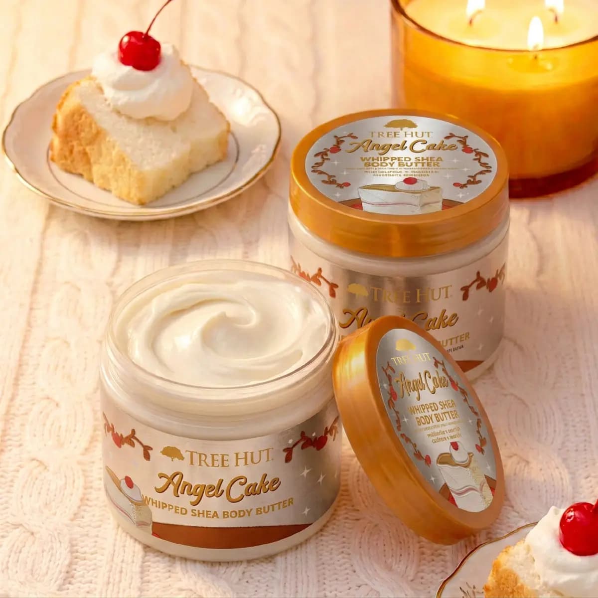 Two Angel Cake Whipped Shea Body Butter jars, one open showing white cream, beside angel cake and a lit candle
