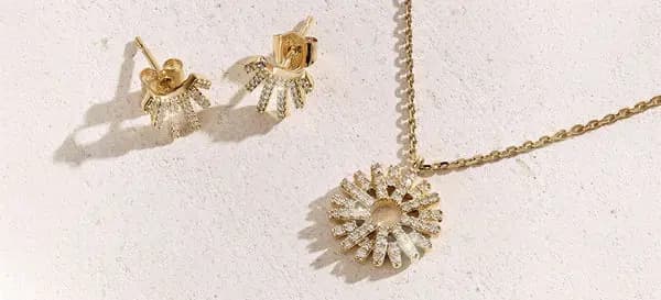 Gold sunburst stud earrings paired with a matching pavé pendant necklace on a cream surface