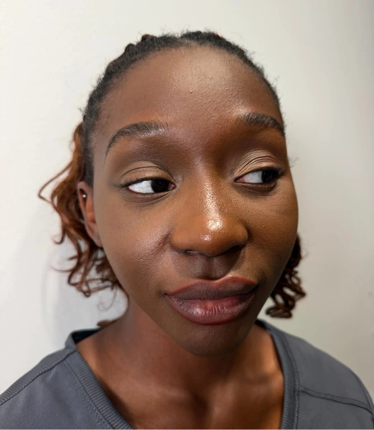 Woman with deep skin tone glancing to the side, wearing a sheer brownish-berry lip with defined liner