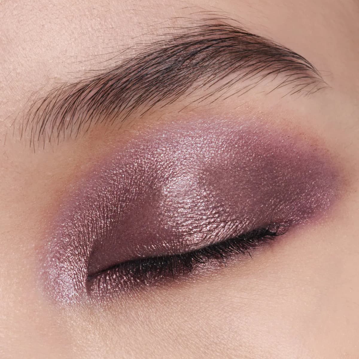 Closed eye with shimmery mauve-violet shadow on the lid, smoked into deeper plum at the outer corner