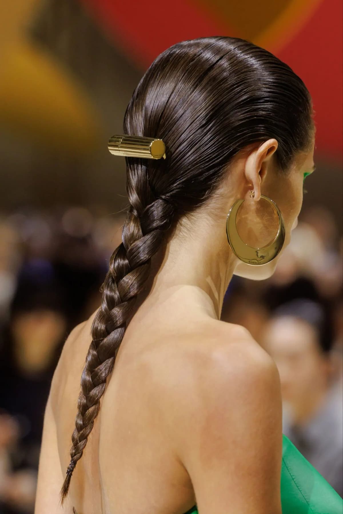 Fluted gold lipstick hair clip on a sleek braid, paired with a large gold Givenchy hoop earring