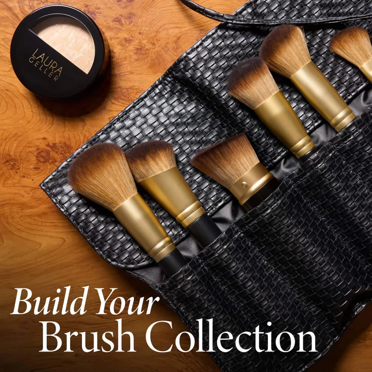 Brushes in an open black woven roll on a wood table beside a Laura Geller baked powder compact, text Build Your Collection