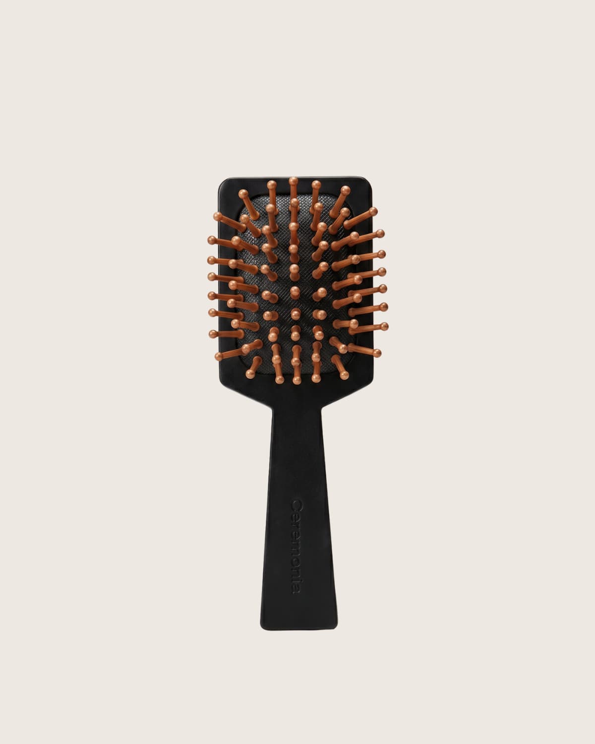 Black Ceremonia mini paddle brush with copper ball-tipped pins on a cream background