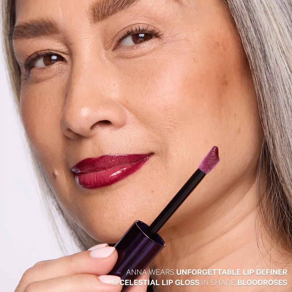 Model holding the gloss doe-foot applicator, lips in shiny berry wine from lip definer and Celestial Lip Gloss