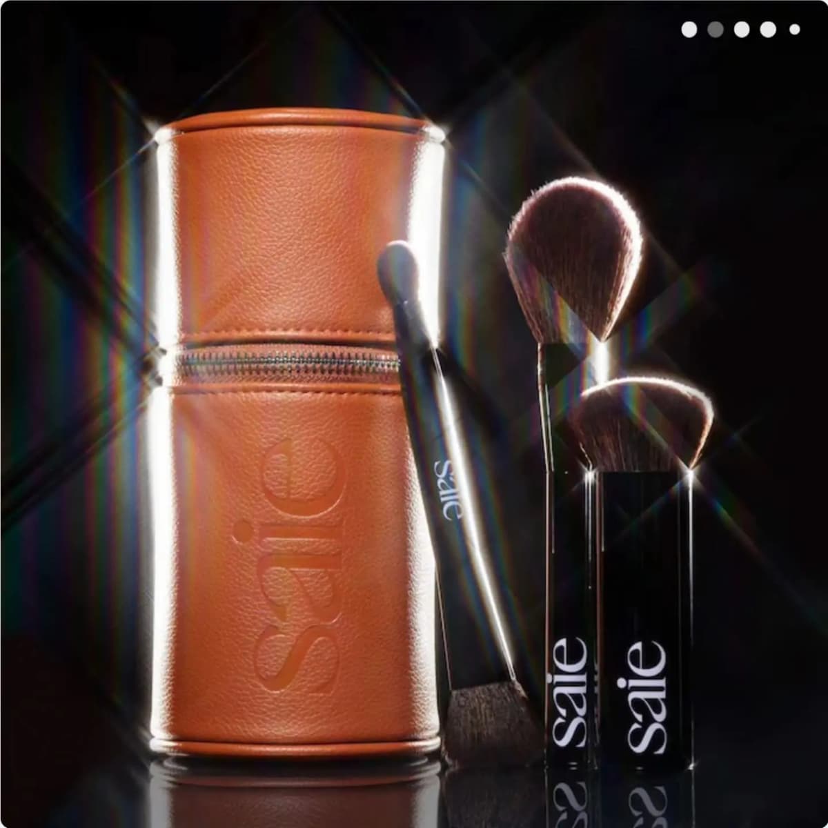 Tan Saie-embossed case and black brushes lit dramatically with starburst flares on a dark backdrop