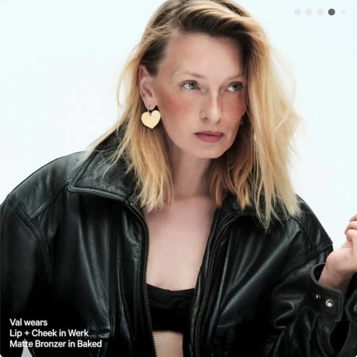 Blonde model Val in a black leather jacket and heart earring wearing Lip + Cheek in Werk and Matte Bronzer in Baked