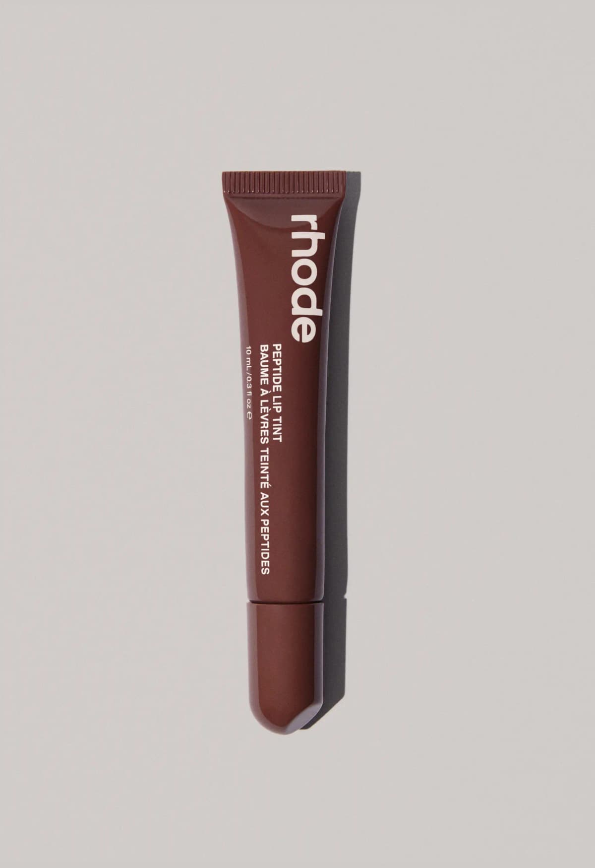 Chocolate-brown rhode lip tint tube with white logo and angled applicator cap on a grey background
