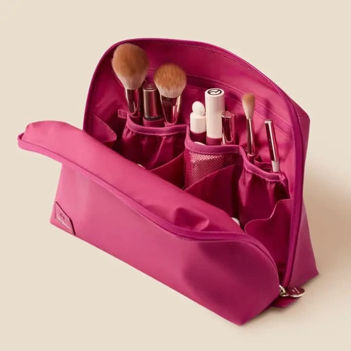 Open raspberry makeup case with elastic pockets holding brushes, lip products and a mesh section
