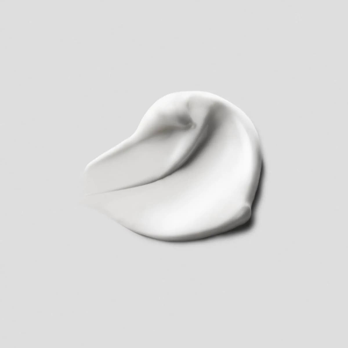 Glossy white cream swatch swirled into a peaked dollop on a pale grey background