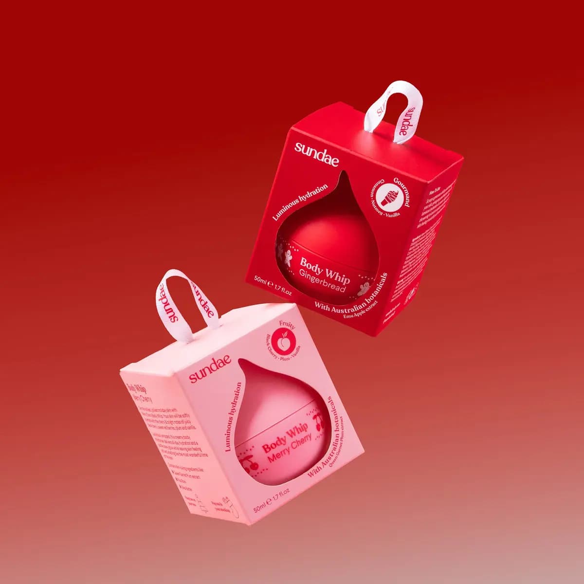 Red Gingerbread and pink Merry Cherry Body Whip boxes with ribbon hangers floating on a red gradient