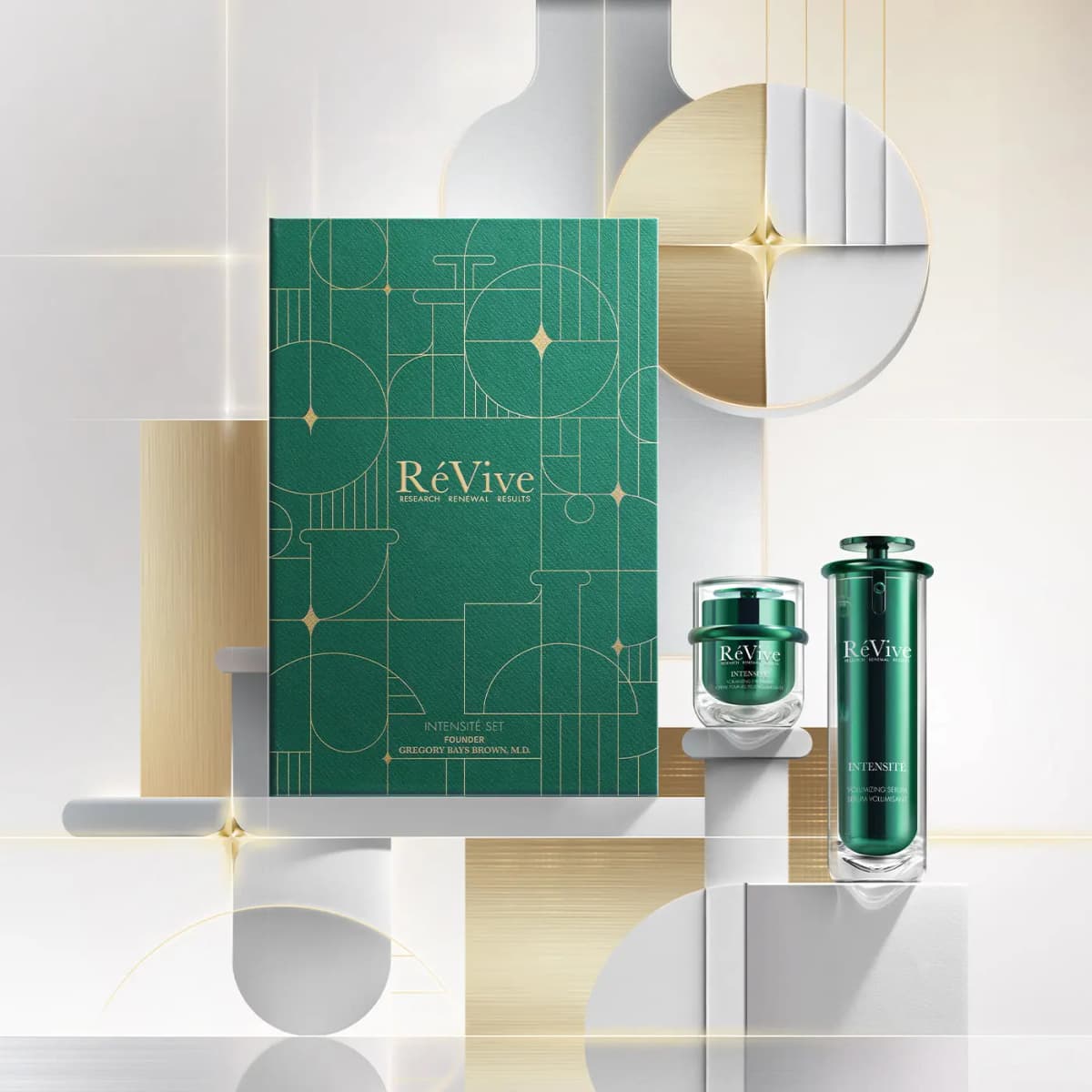 Intensité Set box with eye cream jar and serum on white pedestals against a silver-and-gold geometric backdrop