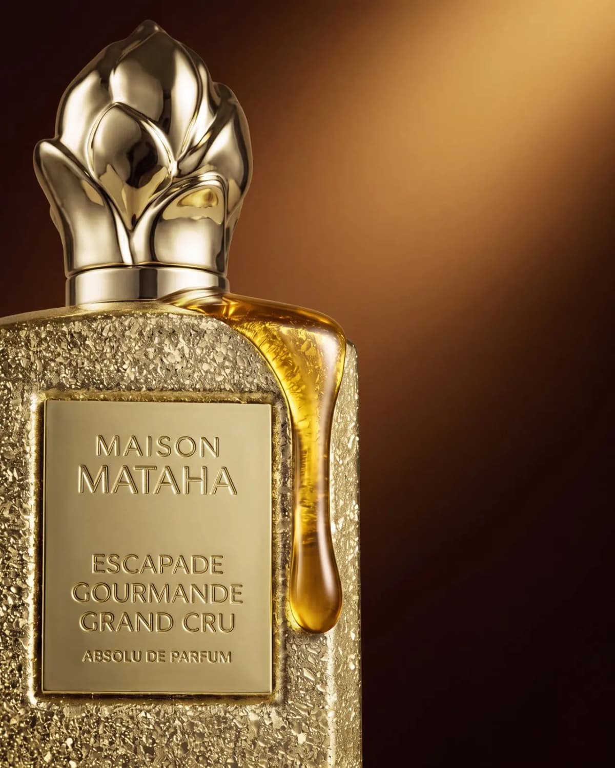 Close-up of sculpted gold flower cap and engraved label with golden syrup dripping down the bottle's side