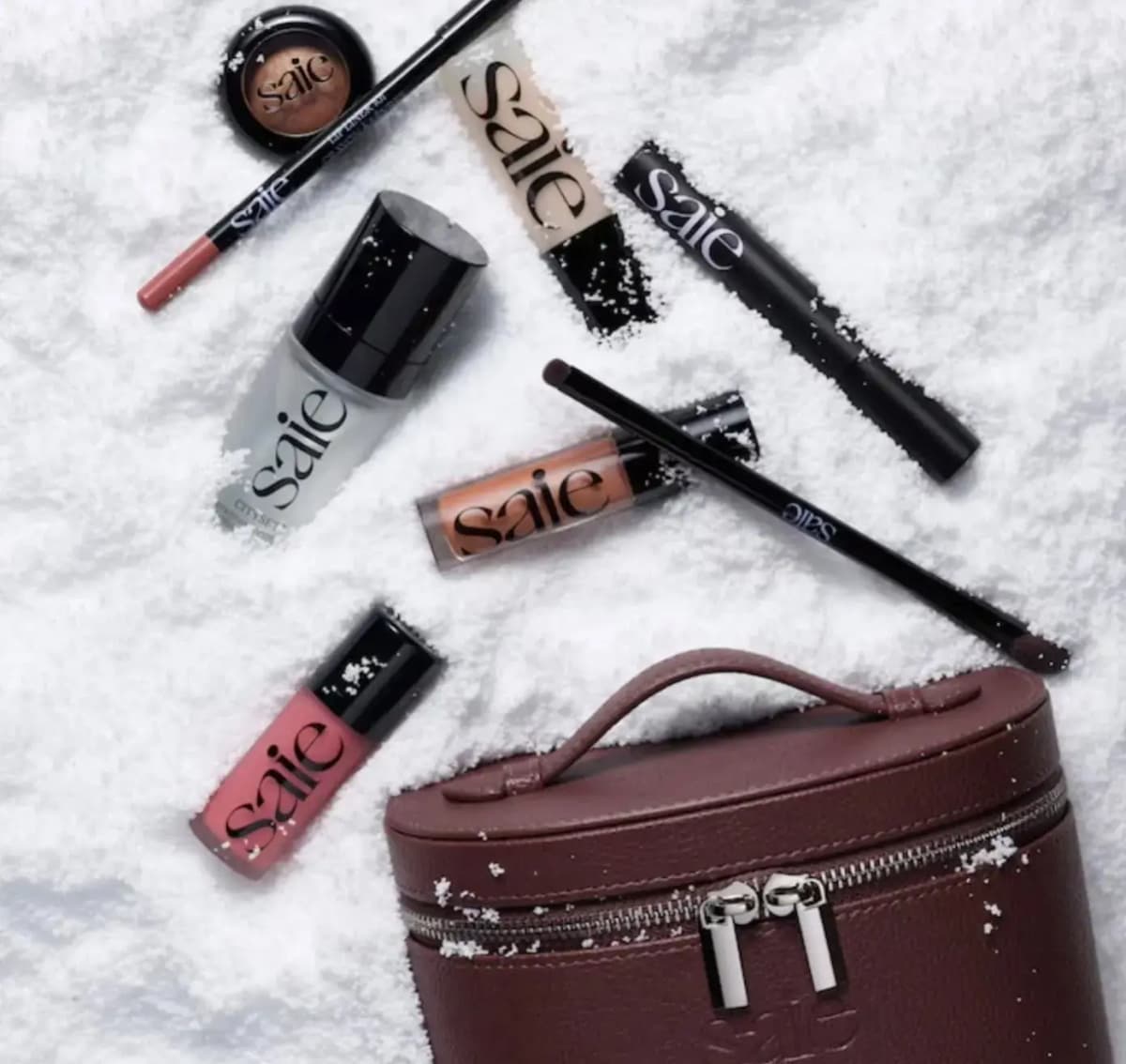 Saie Best of Saie Vault products and burgundy-toned vanity case scattered across white snow