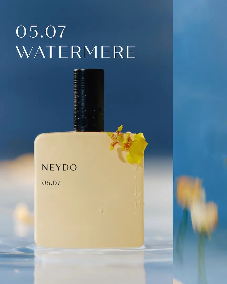 Pale yellow NEYDO 05.07 Watermere bottle with water droplets and a yellow orchid, standing in water against deep blue