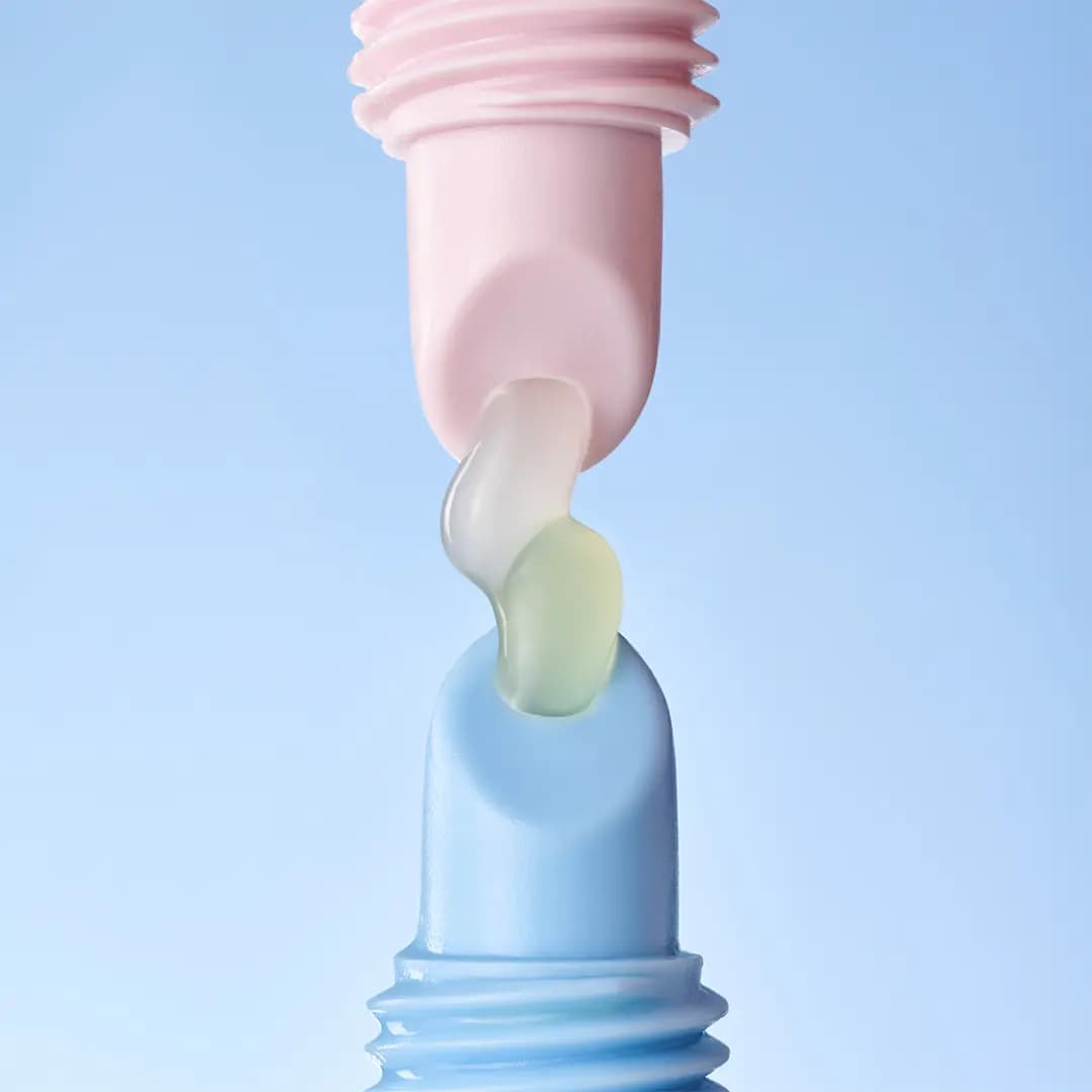 Close-up of pink and blue lip tube tips joined by a translucent, slightly yellow-tinted gloss