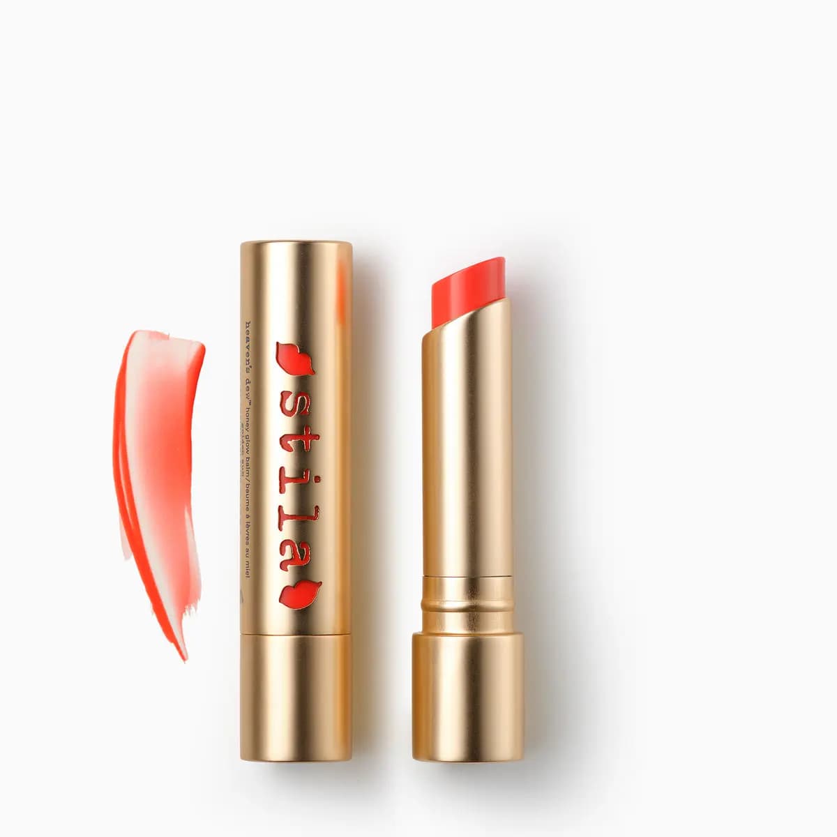 Heaven's dew honey glow balm in coral red, shown open in a gold bullet beside its cap and a sheer swatch