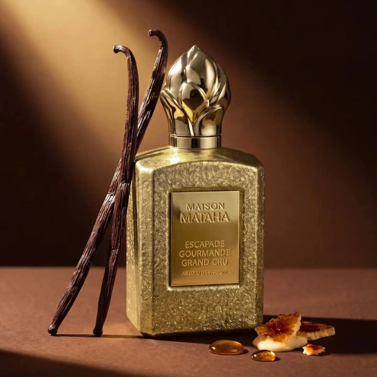 Maison Mataha Escapade Gourmande Grand Cru Absolu de Parfum bottle in textured gold beside vanilla pods and crème brûlée