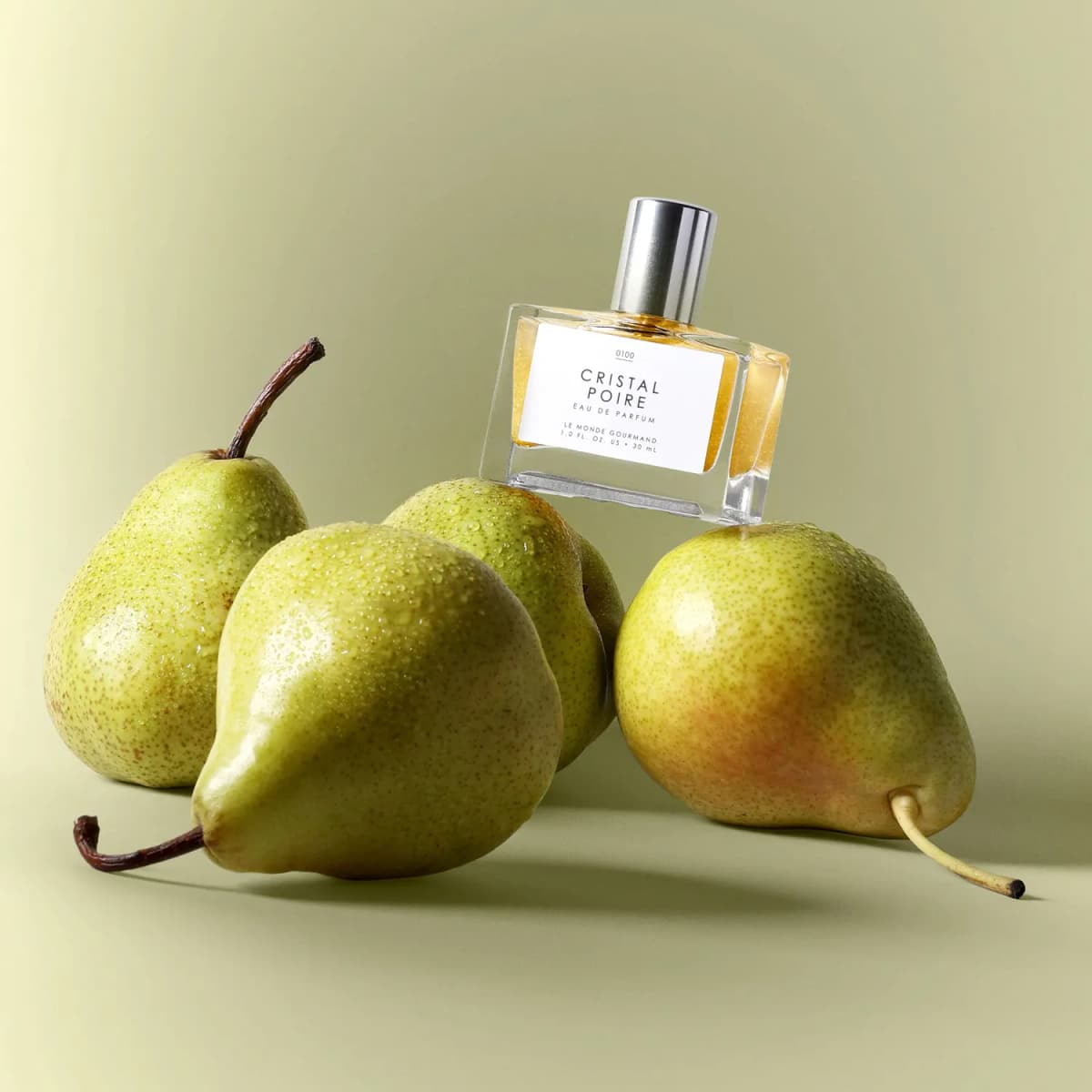 Bottle balanced on four dewy green pears against a soft sage-green backdrop