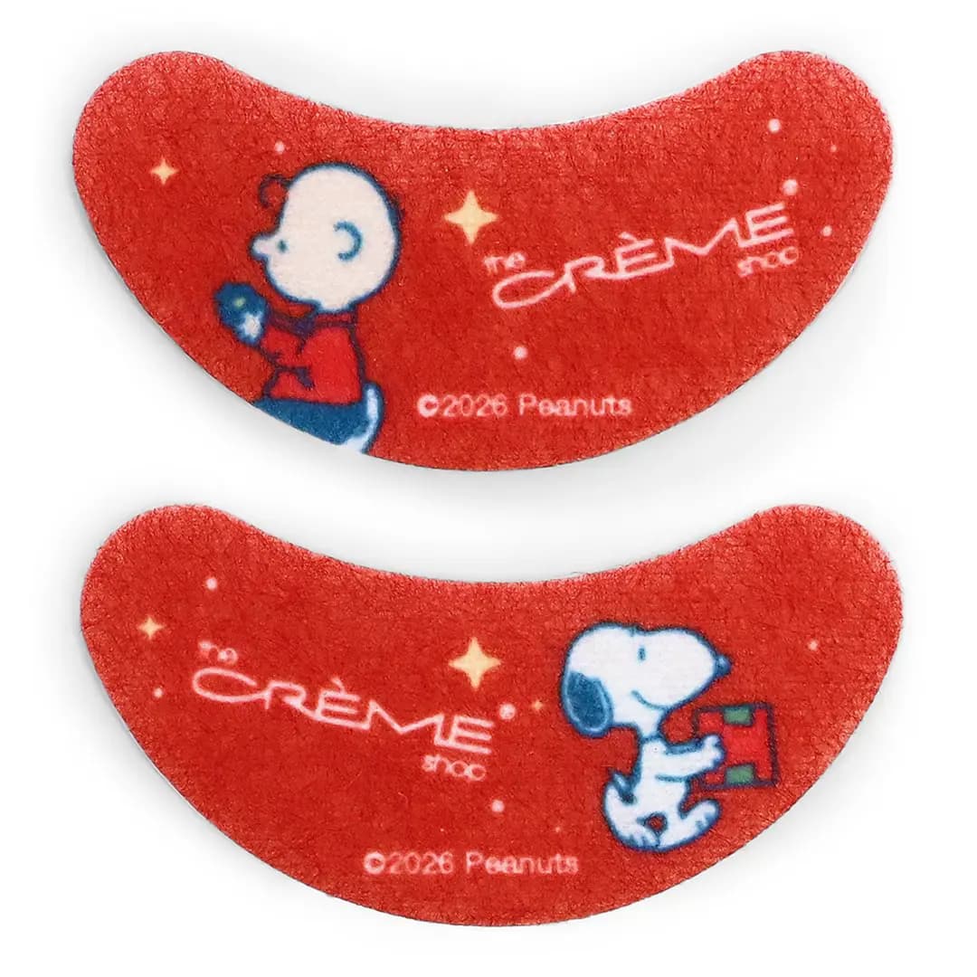 Two red fibre undereye patches printed with Charlie Brown, Snoopy carrying a gift and The Crème Shop logo.