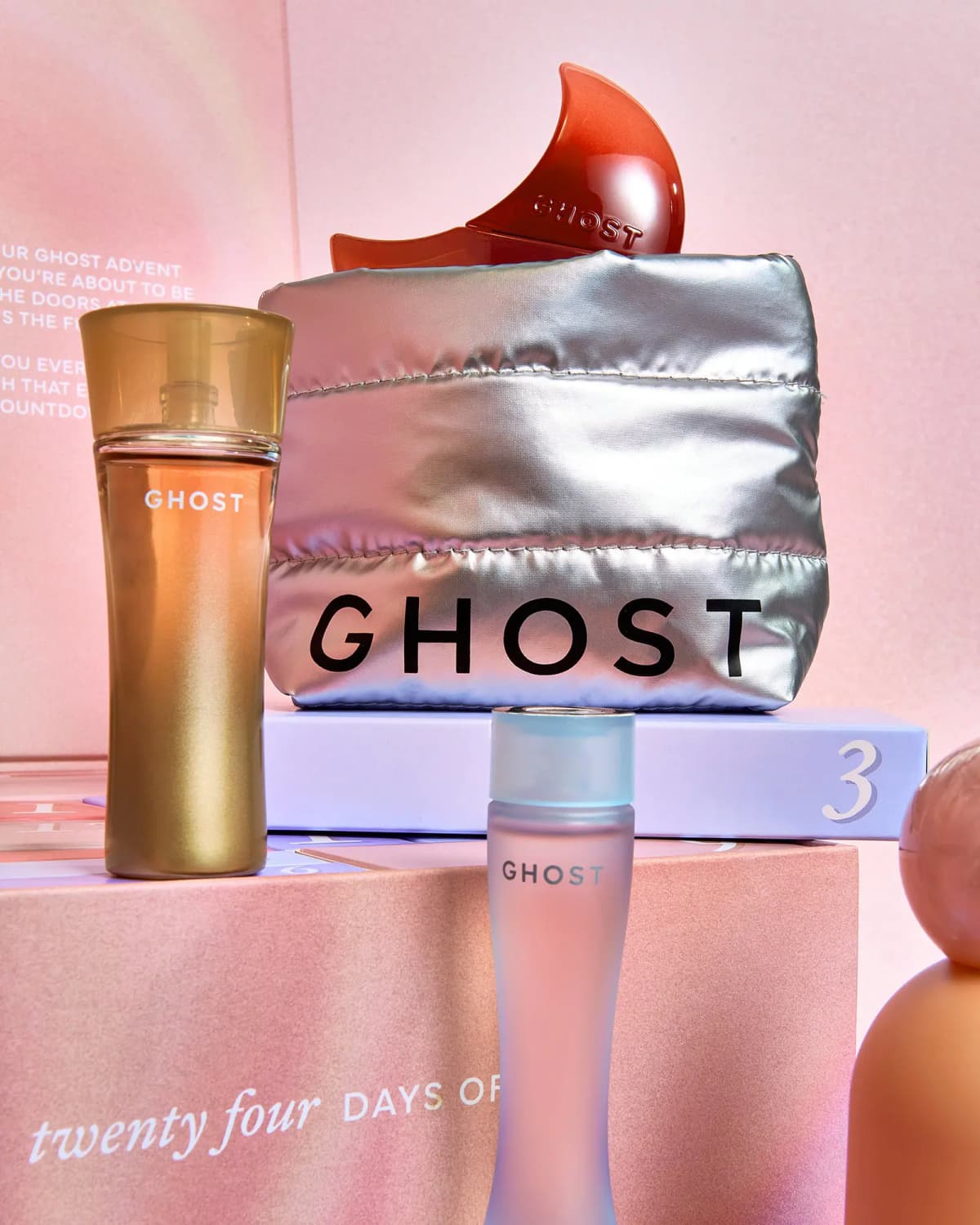Gold and frosted blue Ghost perfume bottles beside a silver Ghost puffer pouch topped with a red moon bottle