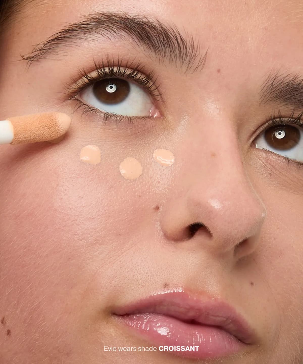 Close-up of three concealer dots under the eye applied with a doe-foot tip, shade Croissant