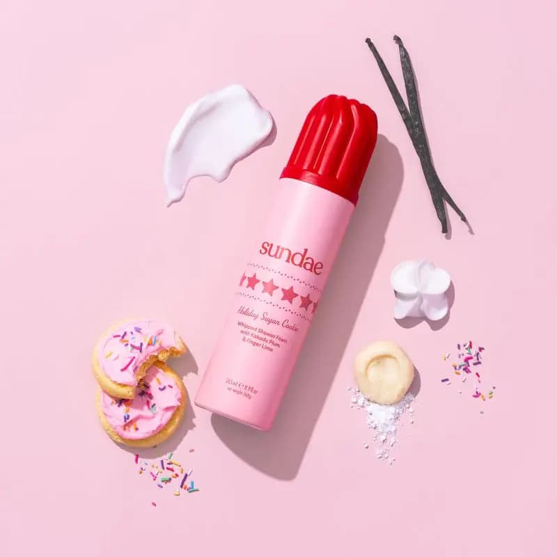 Pink Holiday Sugar Cookie can with frosted sprinkle cookies, vanilla pods and a white foam swatch on pink