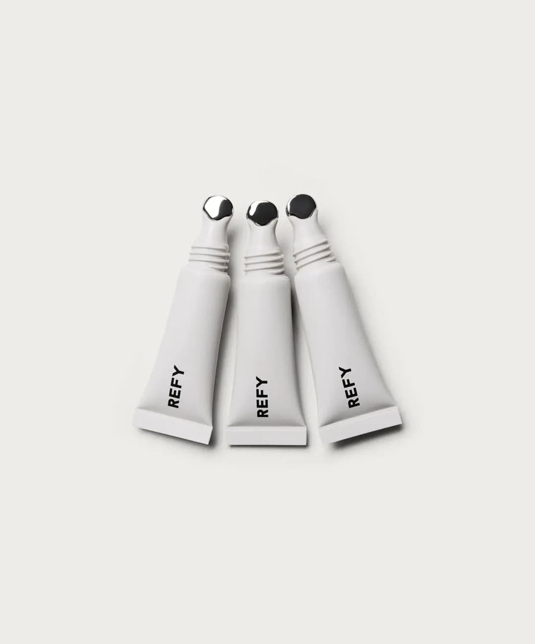 Three white REFY mini lip gloss tubes with silver metal applicator tips fanned out on a pale background