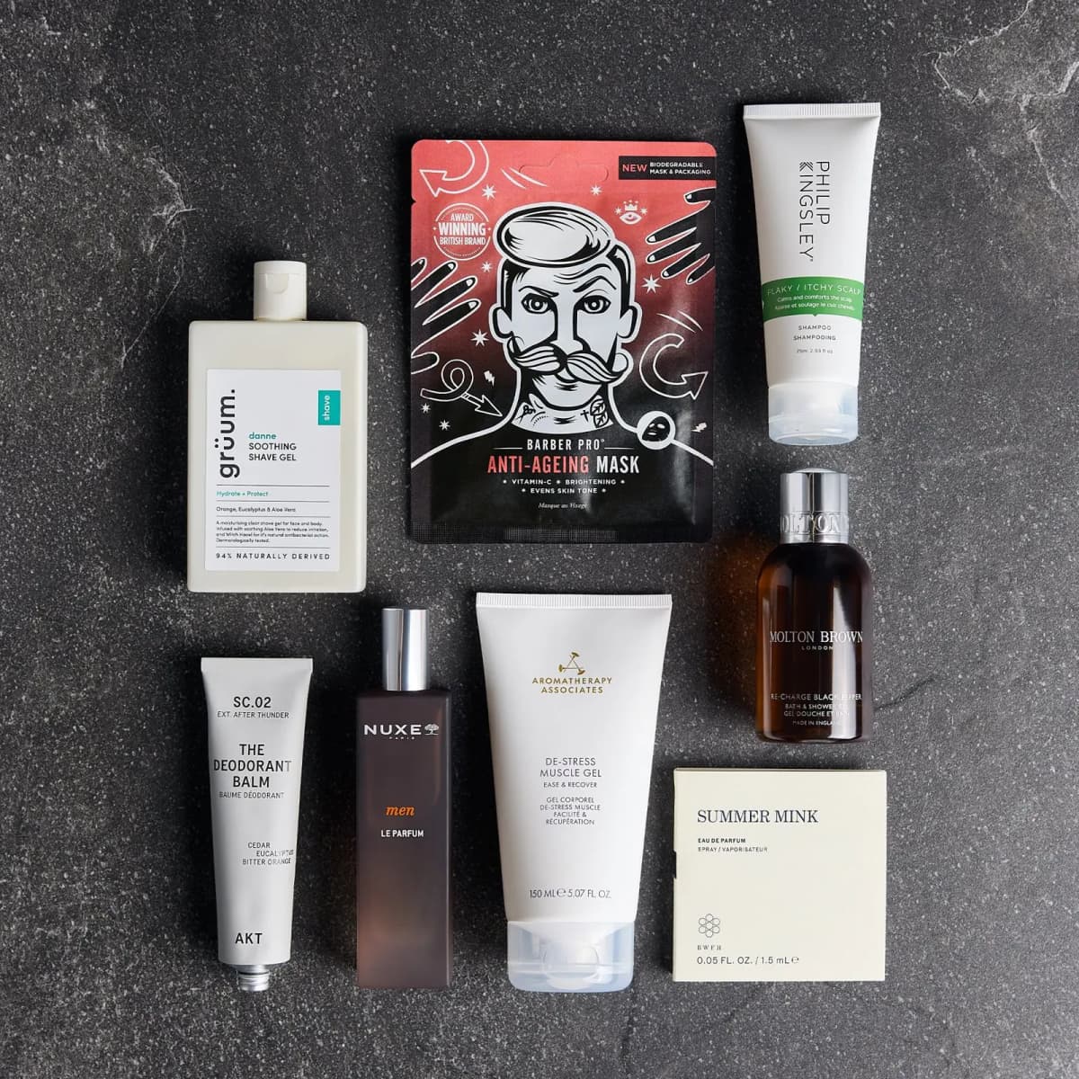 Neat overhead grid of the eight grooming products, including a red Barber Pro mask, arranged on dark grey stone