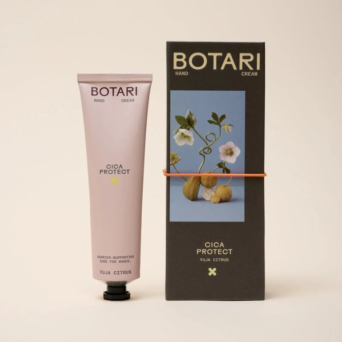 Pale pink BOTARI Cica Protect Yuja Citrus tube next to its dark box showing citrus fruit and hellebores on blue