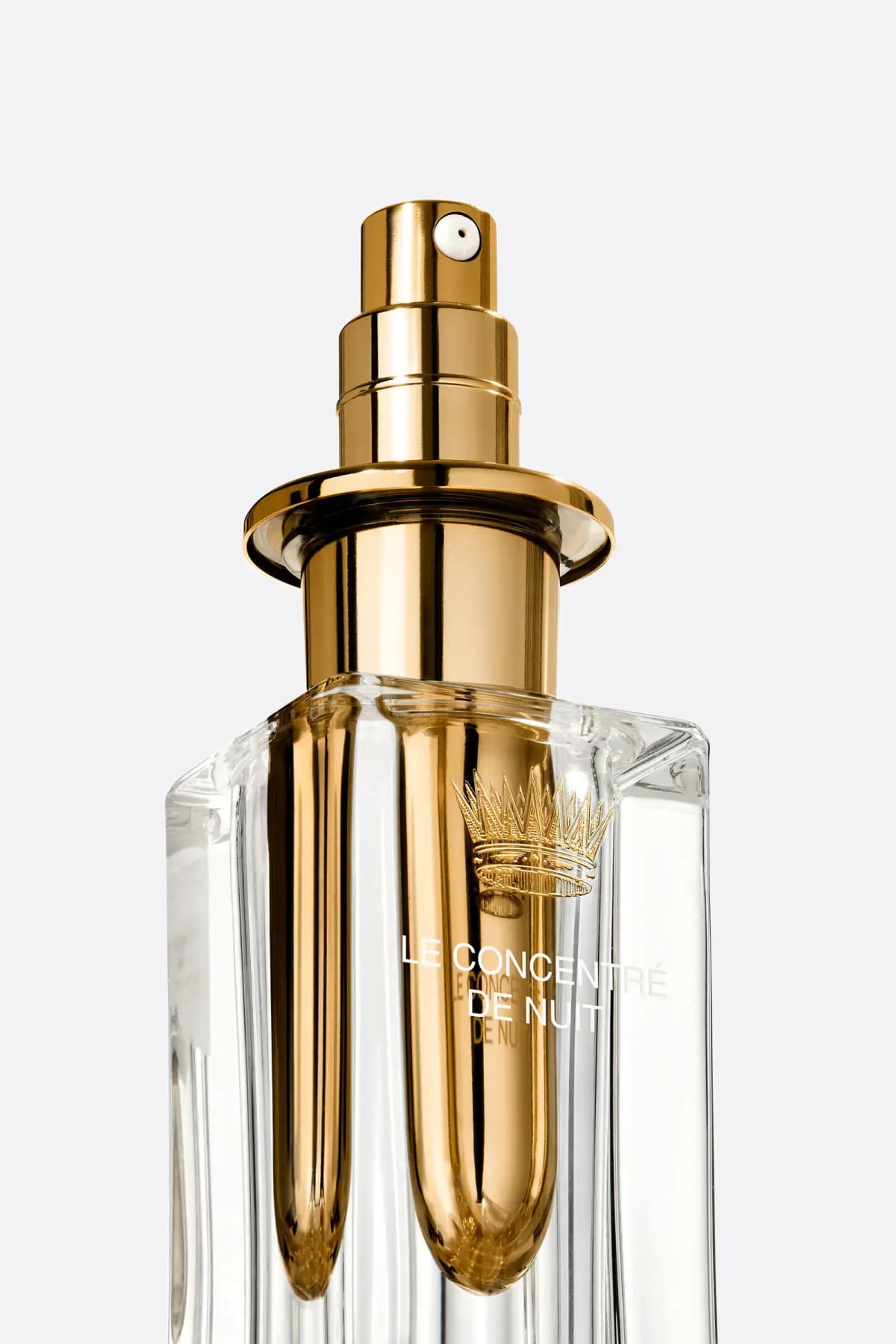 Close-up of gold pump and engraved crown on the inner vial inside the clear faceted glass bottle