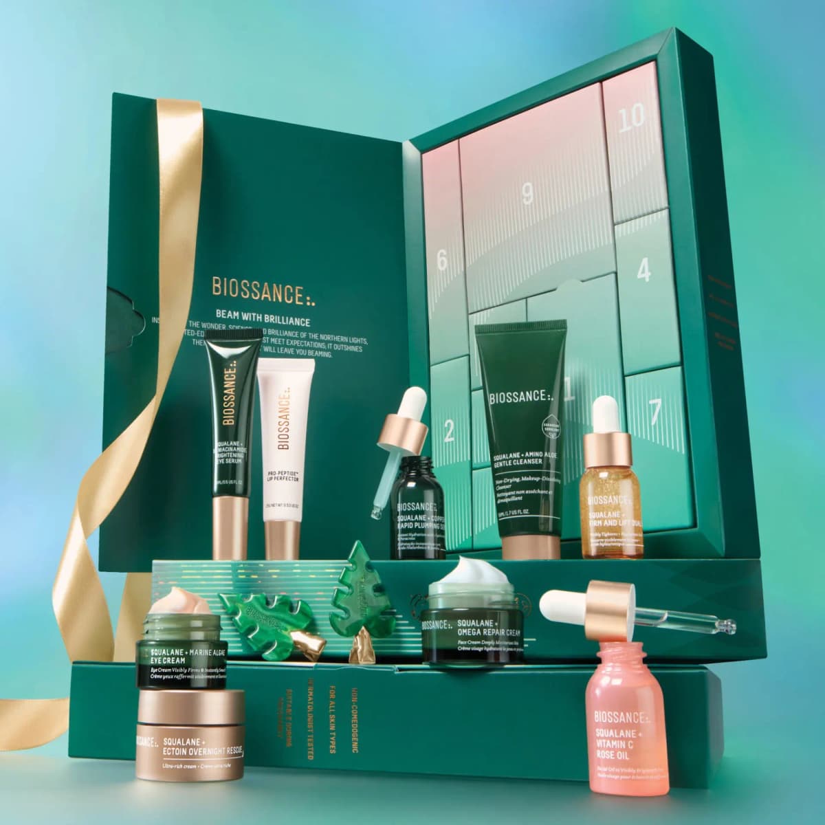 Open teal Biossance advent calendar with pink-to-mint numbered doors, gold ribbon and skincare products arranged in front