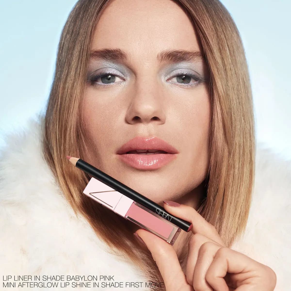 Blonde model in white fur with silvery eyeshadow and glossy pink lip, holding a lip liner and mini pink gloss.