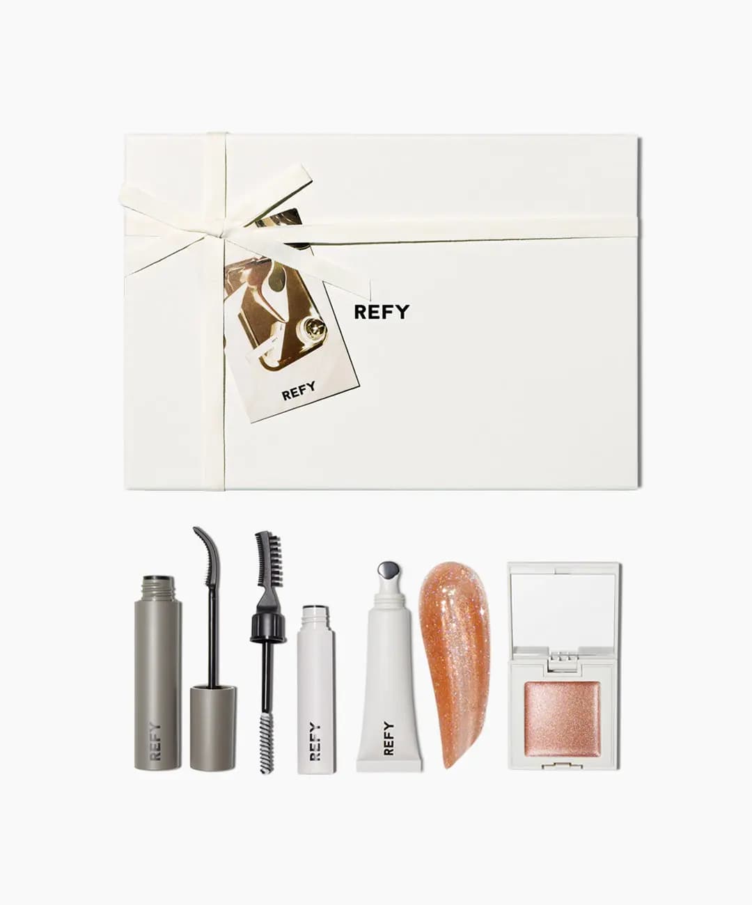 Smaller cream gift box above mascara, brow gel, lip gloss with sparkly peach swatch and rose-gold cream shimmer