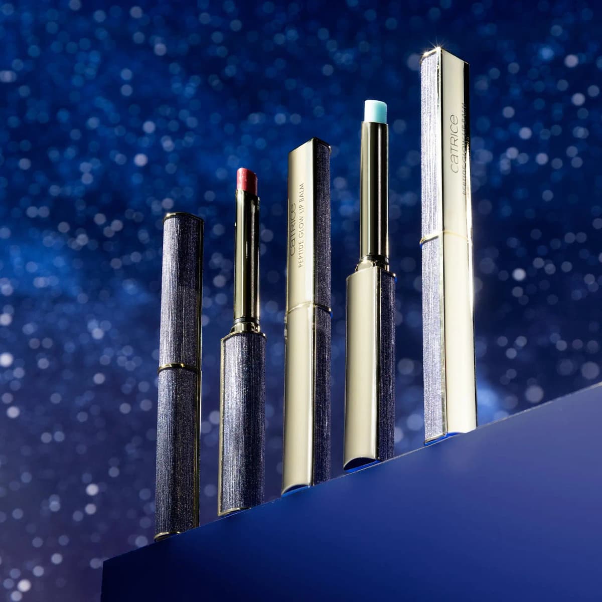 Five glittery navy and gold lip balm tubes, two open showing red and pale-blue bullets, on a blue step