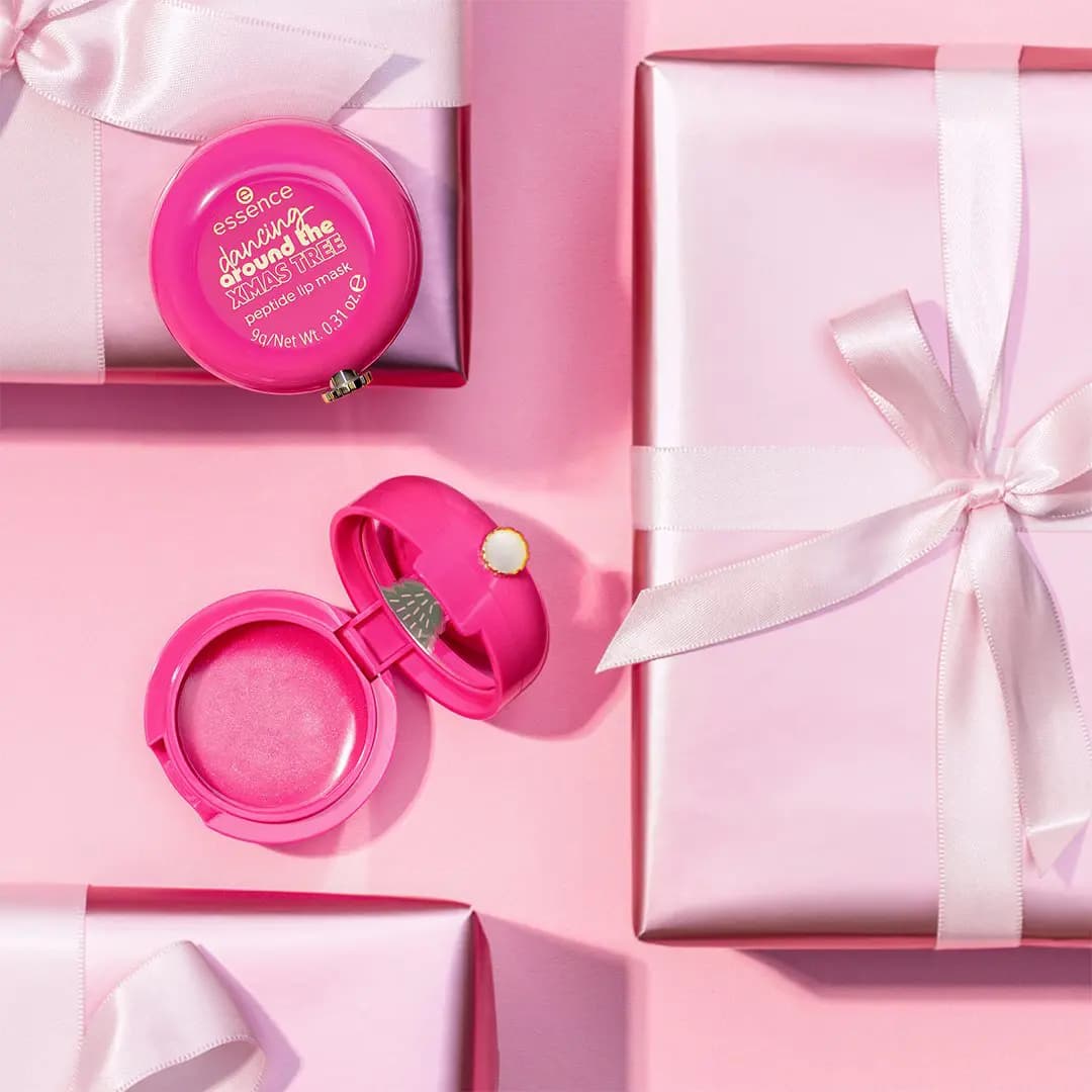 Hot pink peptide lip mask pot, one open showing shimmery pink balm, among pink satin-wrapped gifts