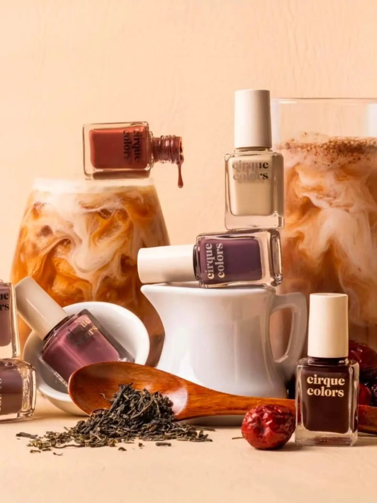 Brown, plum, cream and dark brown polishes with iced milk tea, a white jug, loose tea leaves and a wooden spoon