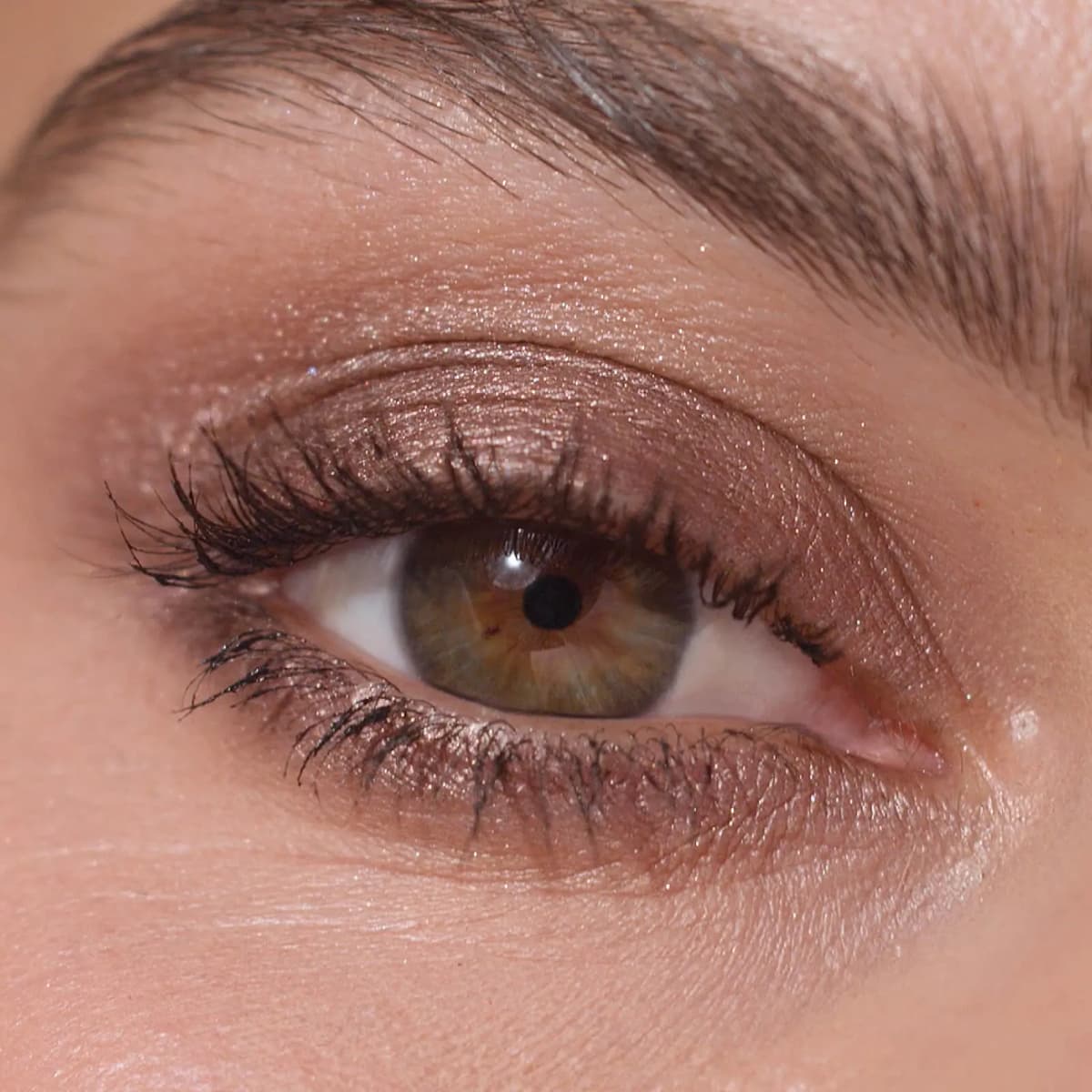 Close-up of a hazel eye wearing warm grey-brown shimmer liner smudged along upper and lower lash lines