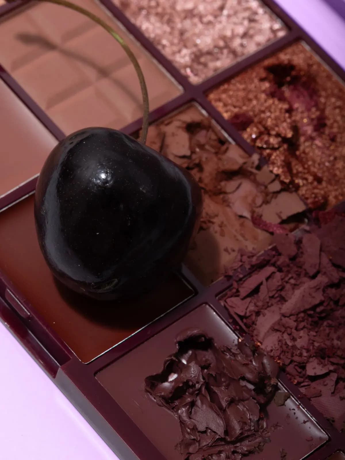 Close-up of crushed brown, mauve and copper shimmer eyeshadows in a burgundy palette with a dark cherry resting on top