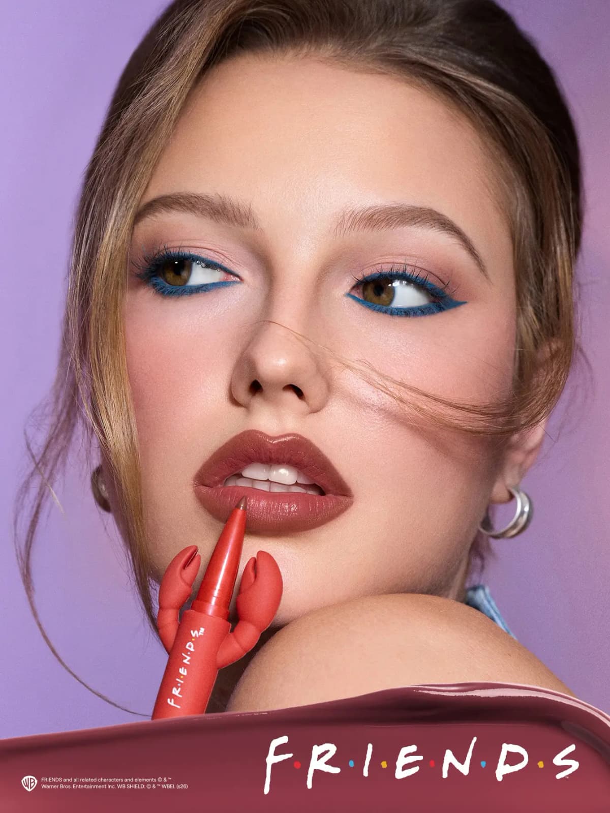 Model with teal winged eyeliner and brown-rose lips holds the red lobster lip duo against a purple backdrop