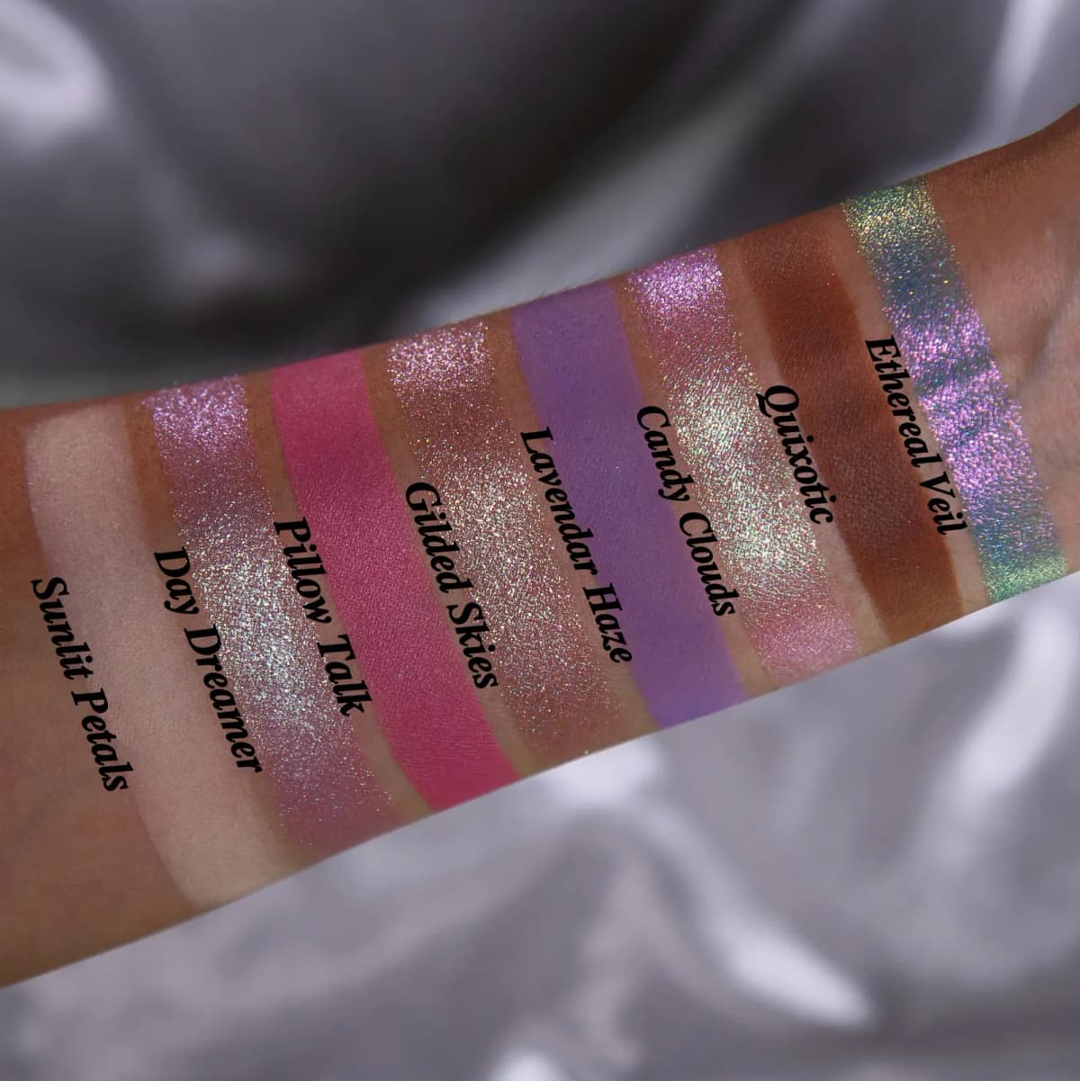 Swatches on deeper skin tone labeled Sunlit Petals through Ethereal Veil against a silver satin background