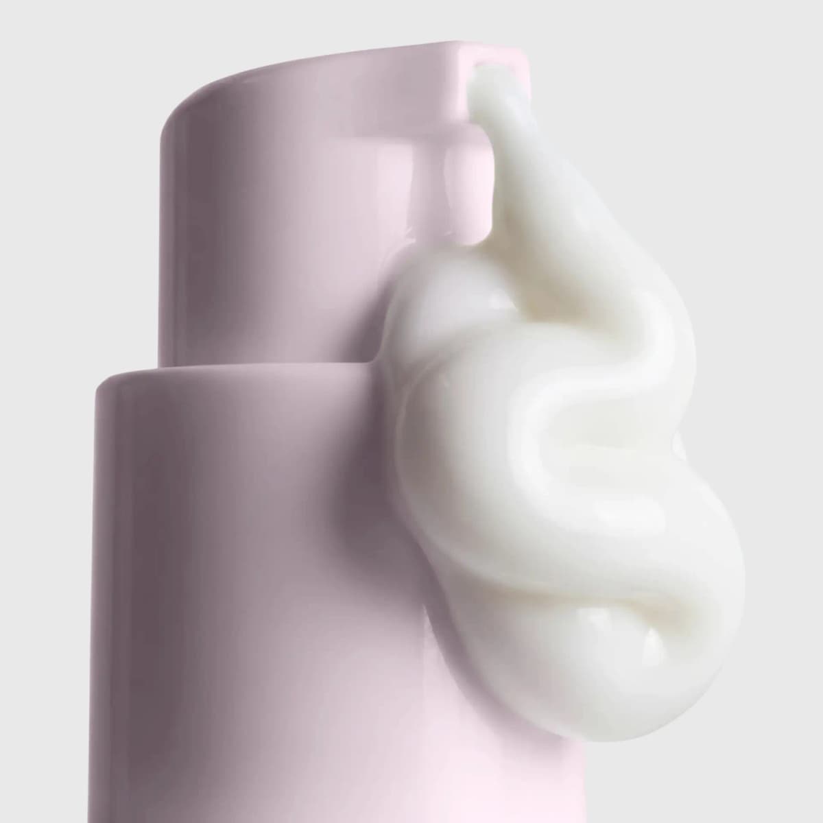 Glossy white primer cream curling in an S-shape beside the pink bottle's pump nozzle