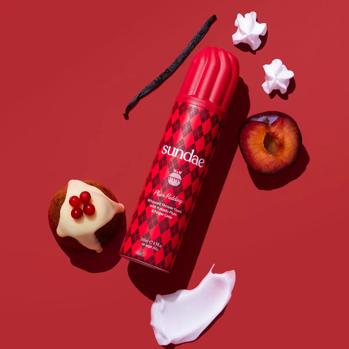 Red argyle Plum Pudding can on red with halved plum, vanilla pod, iced pudding with berries and foam swirl