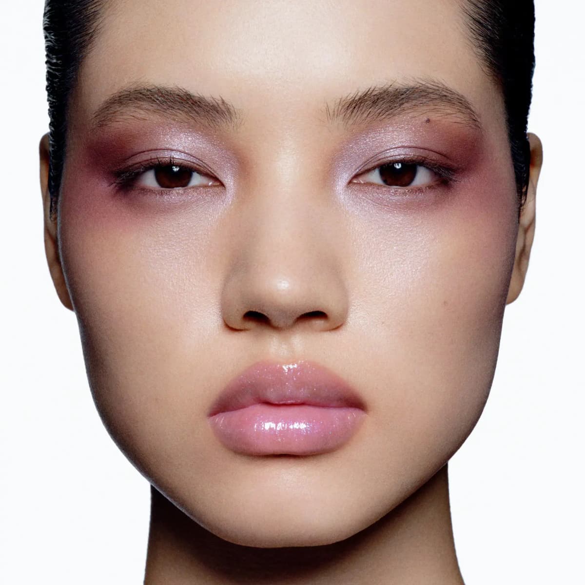 Model with plum-pink eye wash blended into the cheeks, lilac shimmer on lids and glossy pink lips