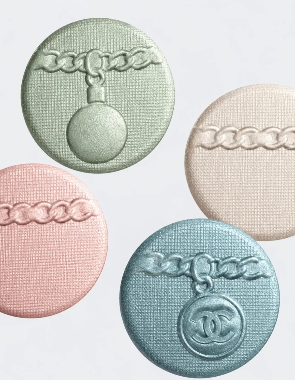 Close-up of four round eyeshadow pans in mint green, cream, pale pink and blue embossed with chain and CC motifs.