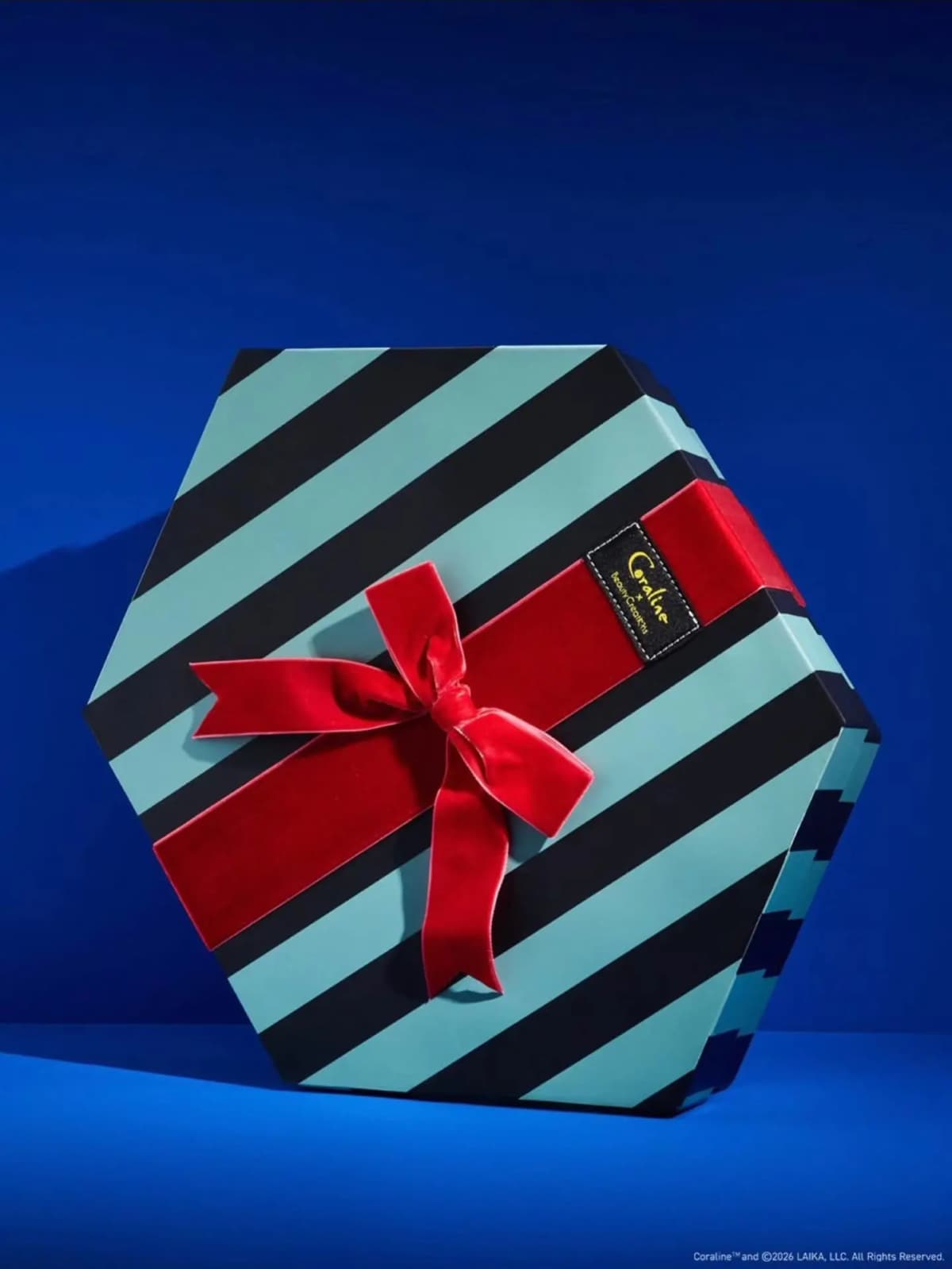 Hexagonal teal and black striped gift box tied with a red velvet bow and Coraline x Beauty Creations label