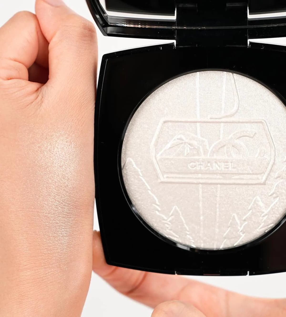 Close-up of Chanel Neige d'Or illuminating powder embossing with a hand swatch