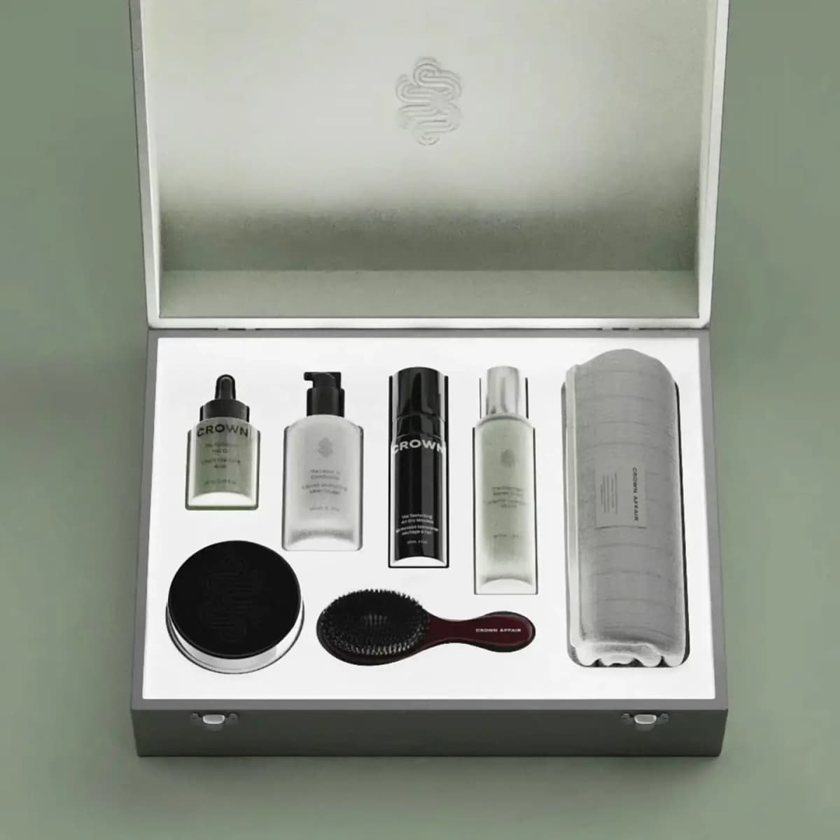 Open grey Crown Affair Vault case with embossed lid, holding oil, leave-in, mousse, serum, jar, burgundy brush