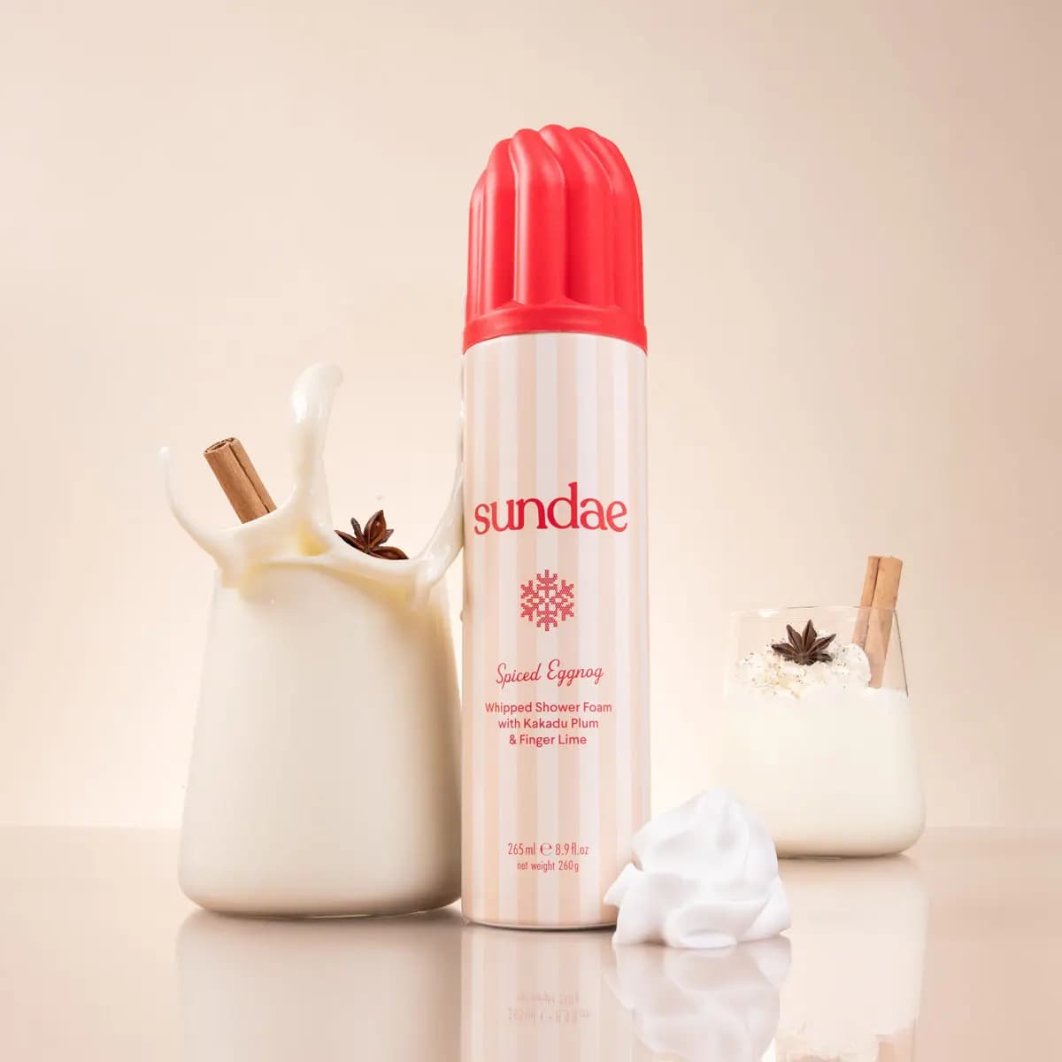 Spiced Eggnog can between a splashing jug of eggnog and a glass topped with cream, star anise and cinnamon